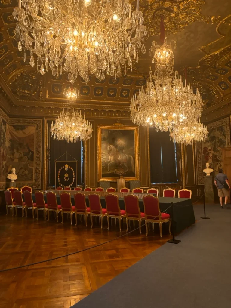 Ornate room inside Stockholm's Royal Palace with chandeliers, tapestries and red chairs