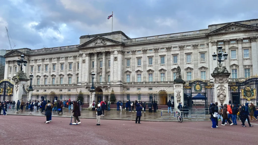 Wide view of Buckingham Palace in London, with its grand architecture and majestic gates, surrounded by lush greenery and the iconic royal residence.