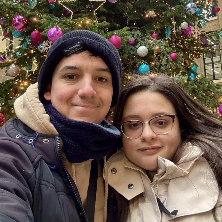 Cyprien and Martina posing in front of a festive Christmas tree in London, surrounded by twinkling lights and holiday cheer.
