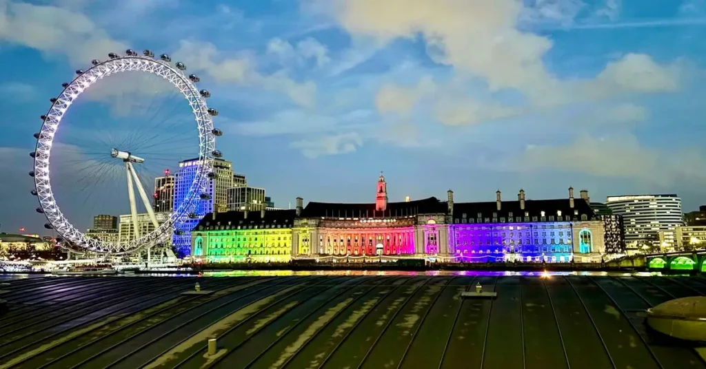 London skyline at night featuring the London Eye illuminated with rainbow colors
