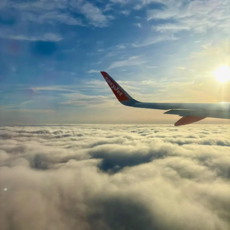 Aerial view from a plane window with the sun shining above the clouds, creating a beautiful golden glow.
