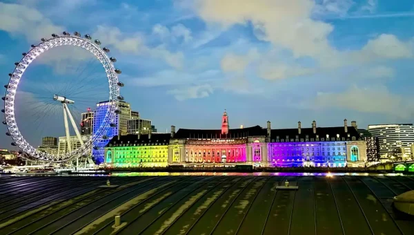 London skyline at night featuring the London Eye illuminated with rainbow colors