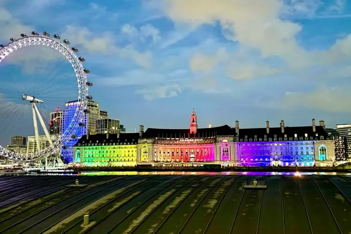 London skyline at night featuring the London Eye illuminated with rainbow colors